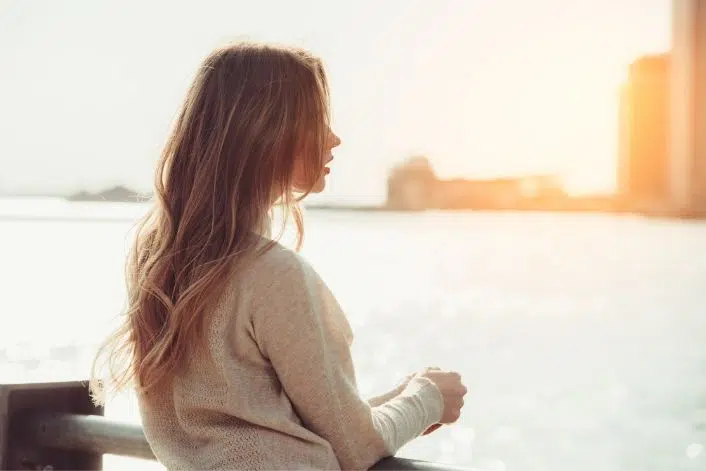 Woman standing outdoors by the water at sunset