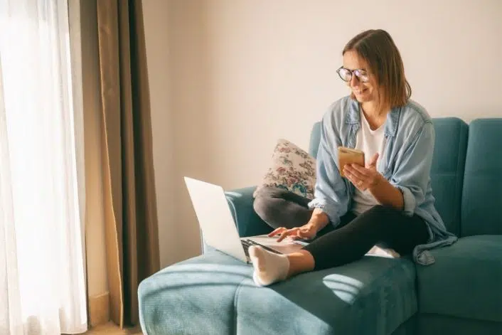 Woman using a laptop and phone while sitting at home