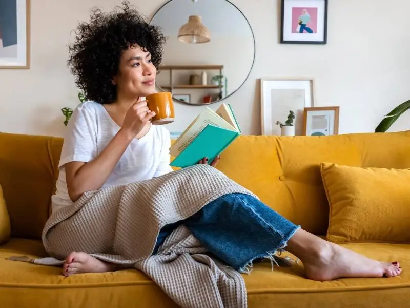 Woman sitting on a couch reading and drinking from a mug
